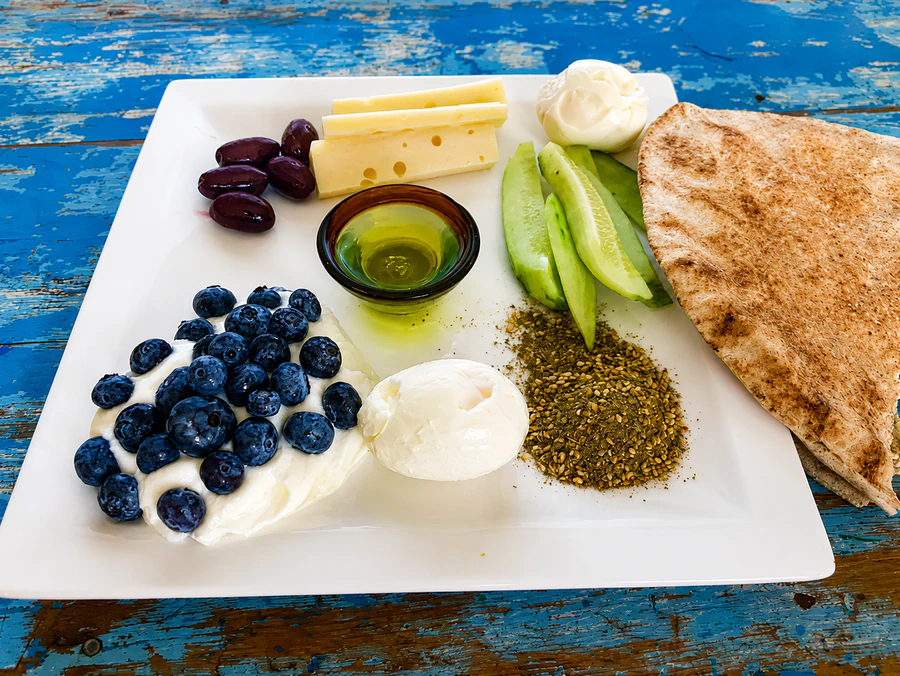 Breakfast plate with blueberries and yogurt, a boiled egg, za'atar, cucumber, and pita