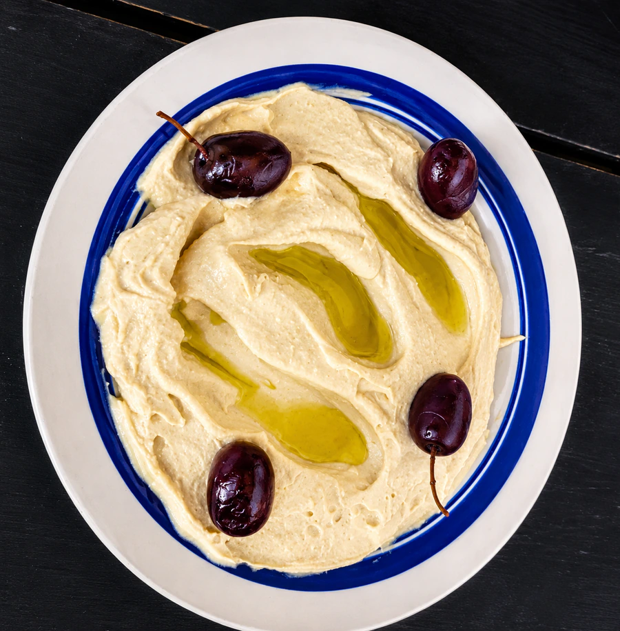 Plate of hummus with olive oil and whole dark olives