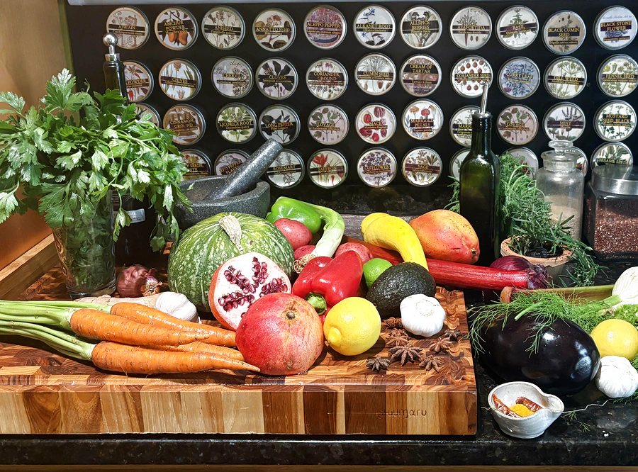 Wall of magnetic spice tins above a kitchen counter with fresh parsley, a mango, and vegetables on a wooden cutting board