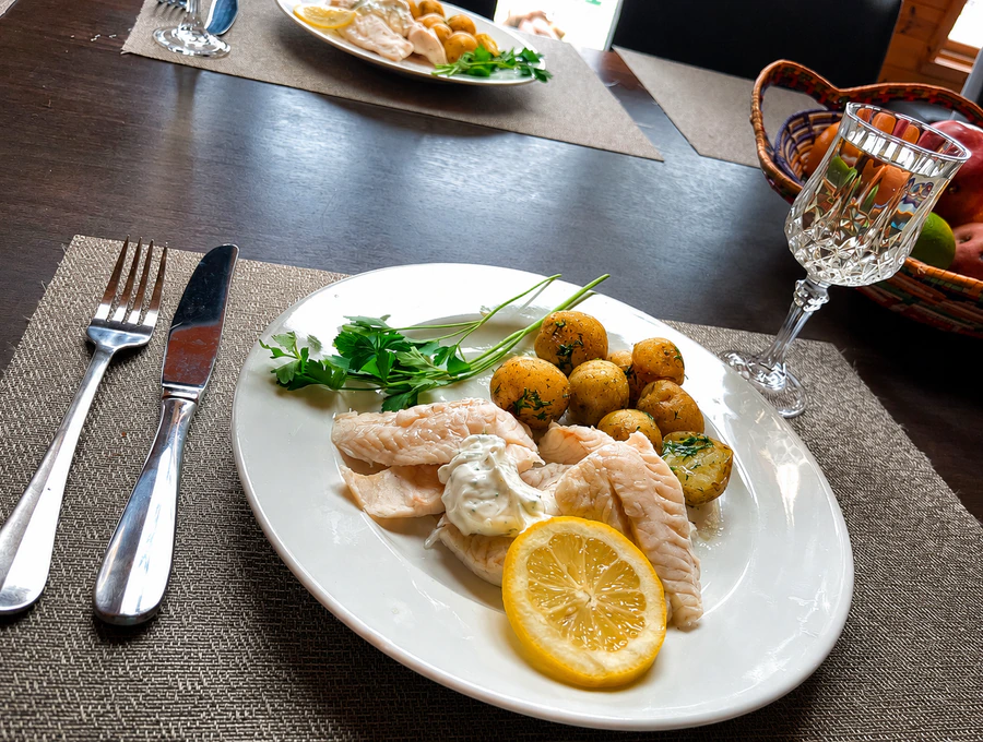 Poached white fish with dill potatoes, a lemon slice, and a glass of white wine